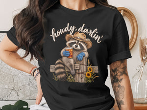 Raccoon in cowboy hat and blue gloves holding drink, with "howdy, darlin'" text.