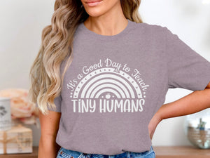 Purple t-shirt with a white rainbow graphic and text that reads "It's a Good Day to Teach TINY HUMANS".