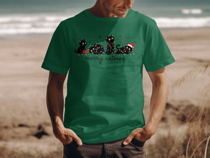 A man wearing a green T-shirt with a graphic of four black cats tangled in Christmas lights and the text merry catmas.