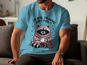 Raccoon in pink scarf holding coffee mug with text "I'm here, I'm awake, don't push it."