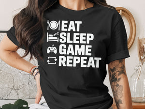 Black t-shirt with white text "Eat Sleep Game Repeat" and icons of a plate, bed, controller, and refresh symbol.