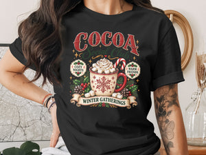 Black t-shirt with "Cocoa Social Club" design featuring a mug of hot cocoa and winter motifs.