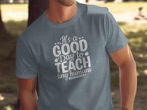 T-shirt with white text: "It's a GOOD Day to TEACH tiny humans" and apple icon.