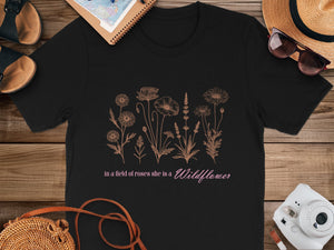 Black t-shirt with line art wildflowers and text: "in a field of roses she is a Wildflower."