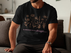 Black t-shirt with a floral line art design and text that reads "in a field of roses she is a Wildflower".