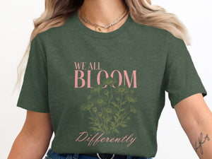 Dark green t-shirt with "WE ALL BLOOM Differently" text and daisy illustration.