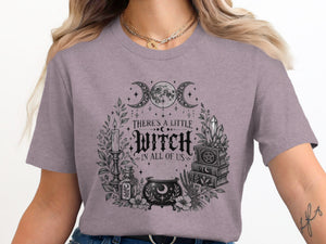 T-shirt graphic with triple moon, cauldron, candles, books, and crystals; text "There's a little witch in all of us."