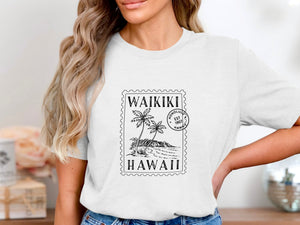 White t-shirt with "Waikiki Hawaii" stamp design featuring palm trees and mountains.