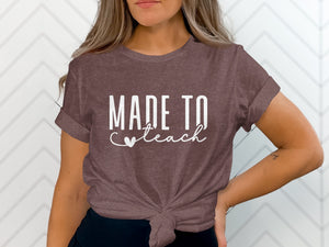 Brown t-shirt on a woman with white text "MADE TO teach" and a heart.