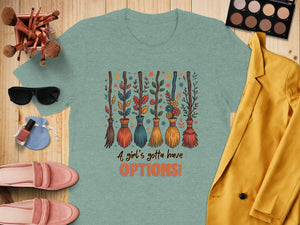 Mint green t-shirt with brooms, leaves, flowers and text: "A girl's gotta have OPTIONS!"