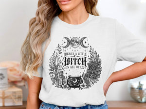 White t-shirt with a black and white witchy graphic and text "There's a little witch in all of us".