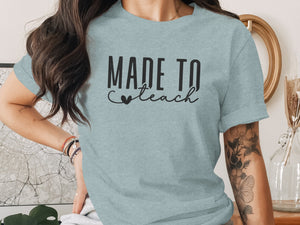Light blue t-shirt with black text reading "MADE TO teach" and a small heart.