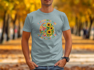 Light blue t-shirt with a circular graphic of a brain half-filled with colorful patterns and half with sunflowers, text reads "THE SUN WILL RISE AND WE WILL TRY AGAIN".