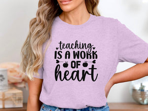Lilac t-shirt with black text: teaching is a work of heart with apples.