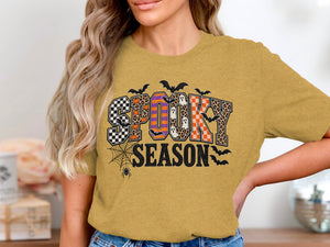 Woman wearing a mustard yellow t-shirt with "SPOOKY SEASON" Halloween graphic.