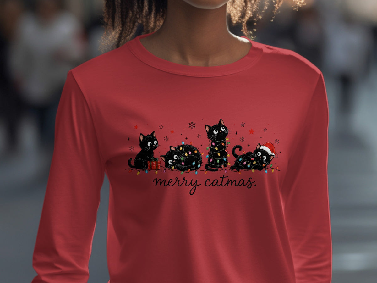 A red long-sleeve shirt with an illustration of four black cats tangled in Christmas lights and the text "merry catmas."