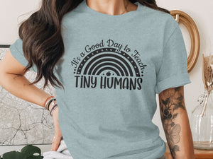 Light blue t-shirt with a rainbow graphic and text "It's a Good Day to Teach Tiny Humans".