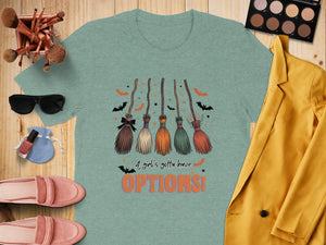 Teal t-shirt with graphic of five brooms, bats, stars, and text "A girl's gotta have OPTIONS!"
