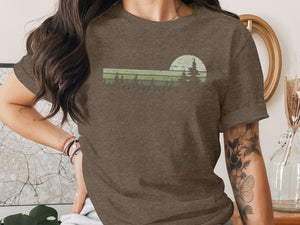 Brown t-shirt with green sunset and pine trees graphic design.