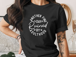 Black t-shirt with white text: "Another fine day ruined by adulthood."
