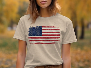 A person wearing a heather beige t-shirt featuring a distressed American flag graphic on the chest.