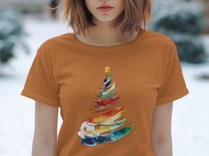 Orange t-shirt with a watercolor Christmas tree design featuring colorful stripes and a star.
