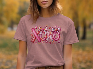 Pink t-shirt with a graphic of "XOXO" made of striped and patterned elements and hearts.