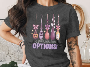 Dark gray t-shirt with a Halloween-themed graphic of brooms, ghosts, and the text "A girl's gotta have OPTIONS!".