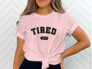 Pink t-shirt with black distressed text reading "TIRED 24/7".
