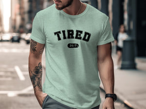 Man in pale green t-shirt with "TIRED 24/7" printed on it.