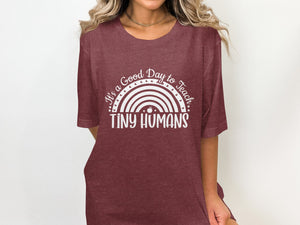 Maroon t-shirt with white text and rainbow graphic that reads "It's a Good Day to Teach Tiny Humans".