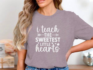 Purple t-shirt with white text "i teach the sweetest little hearts" and an apple.