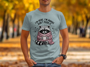Raccoon wearing a pink sweater holding a mug with text "I'M HERE, I'M AWAKE DON'T PUSH IT."