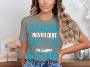 Grey t-shirt with text "GAMERS NEVER QUIT WE SIMPLY RESTART" and a video game controller graphic.