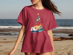 Maroon t-shirt with watercolor Christmas tree graphic on a beach background.