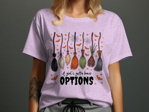 Light purple t-shirt with colorful brooms, bats, spiderwebs, and text "A girl's gotta have OPTIONS".