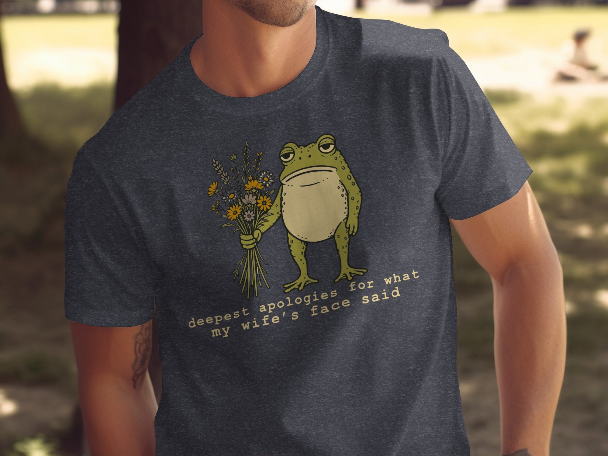 Dark grey t-shirt with a frog holding flowers and the text "deepest apologies for what my wife's face said".
