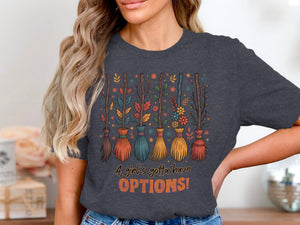 T-shirt with cartoon brooms, autumn leaves, flowers, and text saying "A girl's gotta have OPTIONS!"