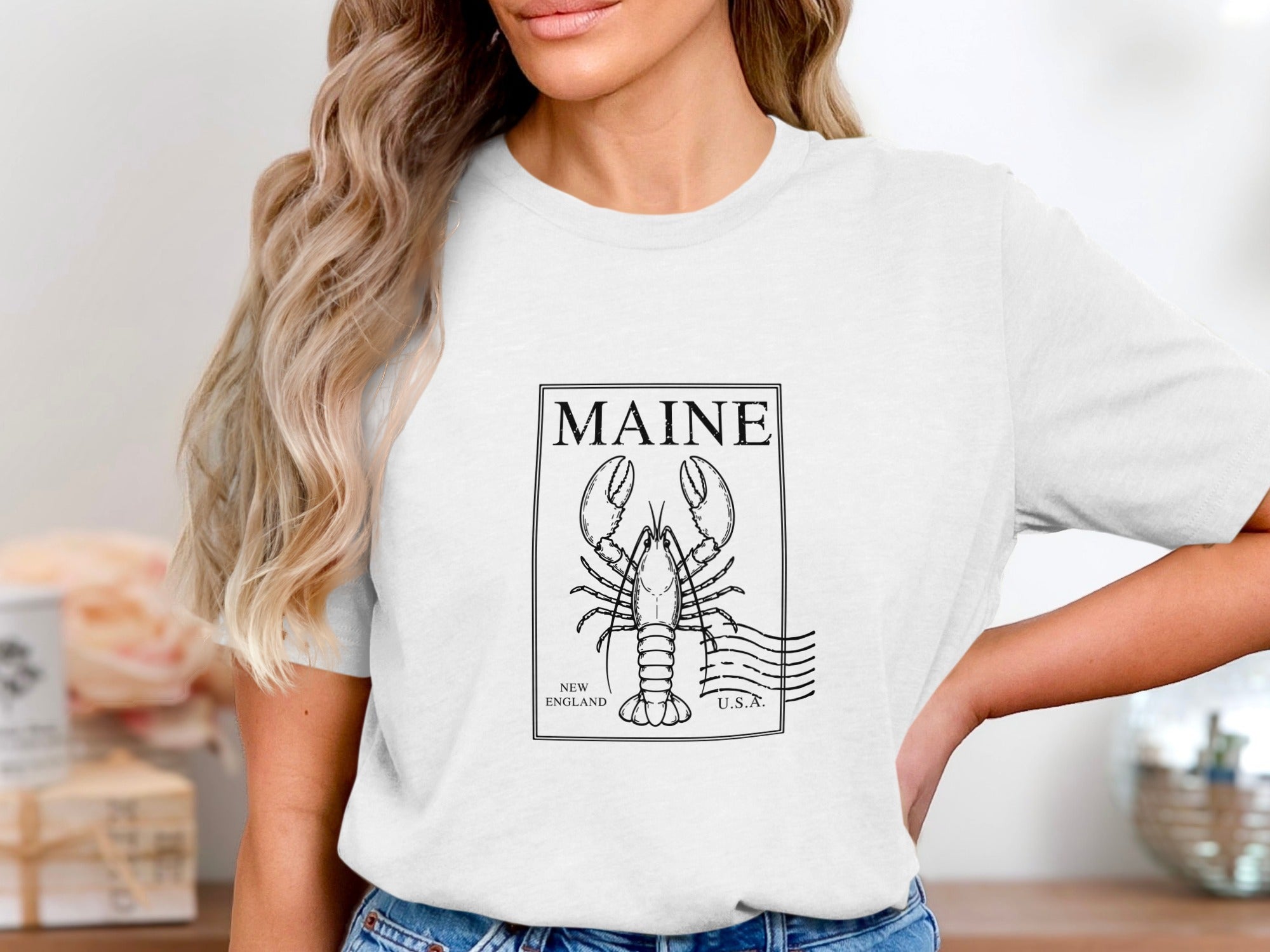 White t-shirt with a black outlined lobster stamp featuring "MAINE", "NEW ENGLAND", and "U.S.A."
