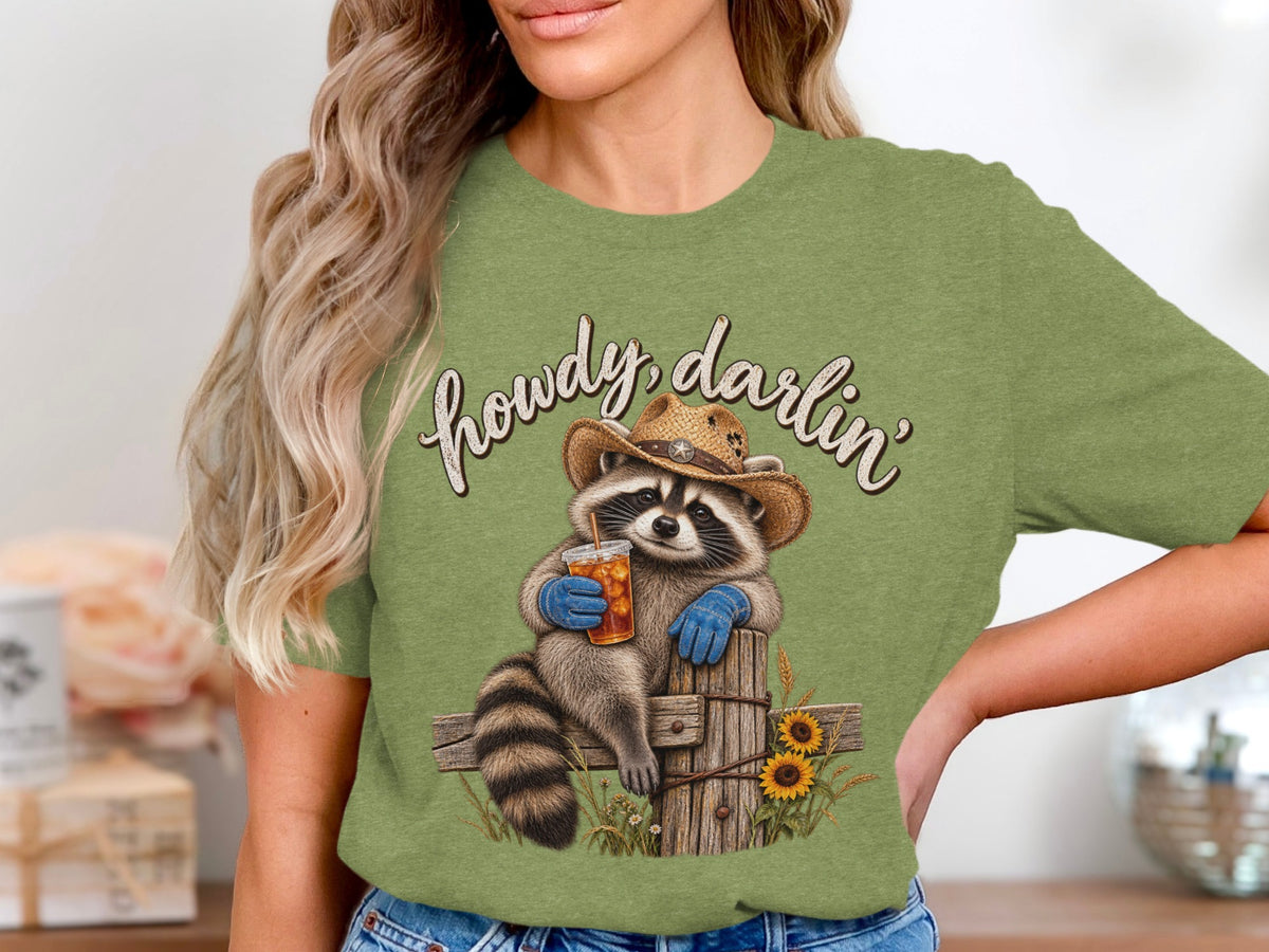 Raccoon in cowboy hat holding drink, text "howdy, darlin'", sunflowers and fence.