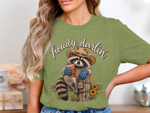 Raccoon in cowboy hat holding drink, text "howdy, darlin'", sunflowers and fence.