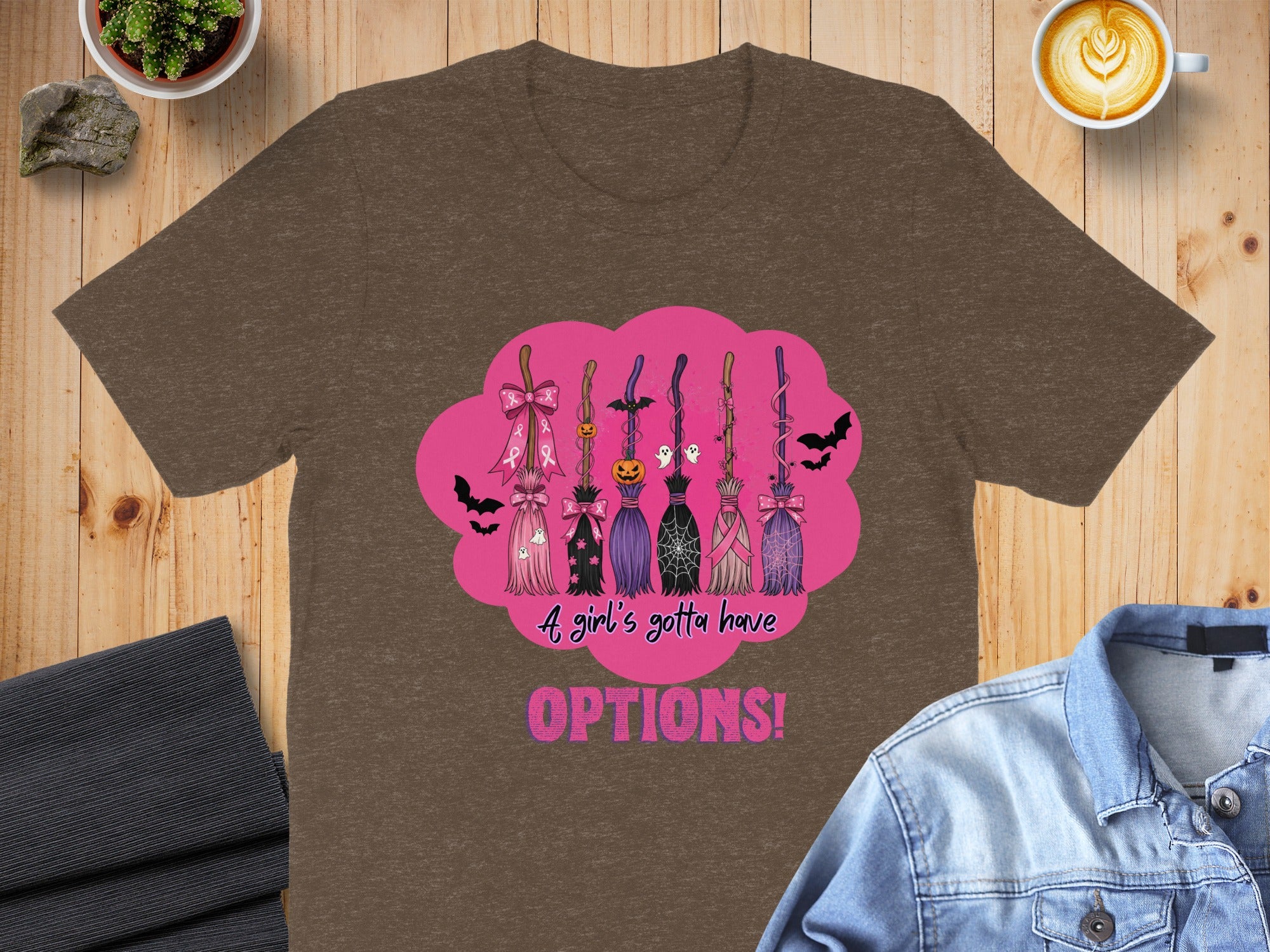 T-shirt with Halloween brooms, pink ribbons, spooky details, and text.