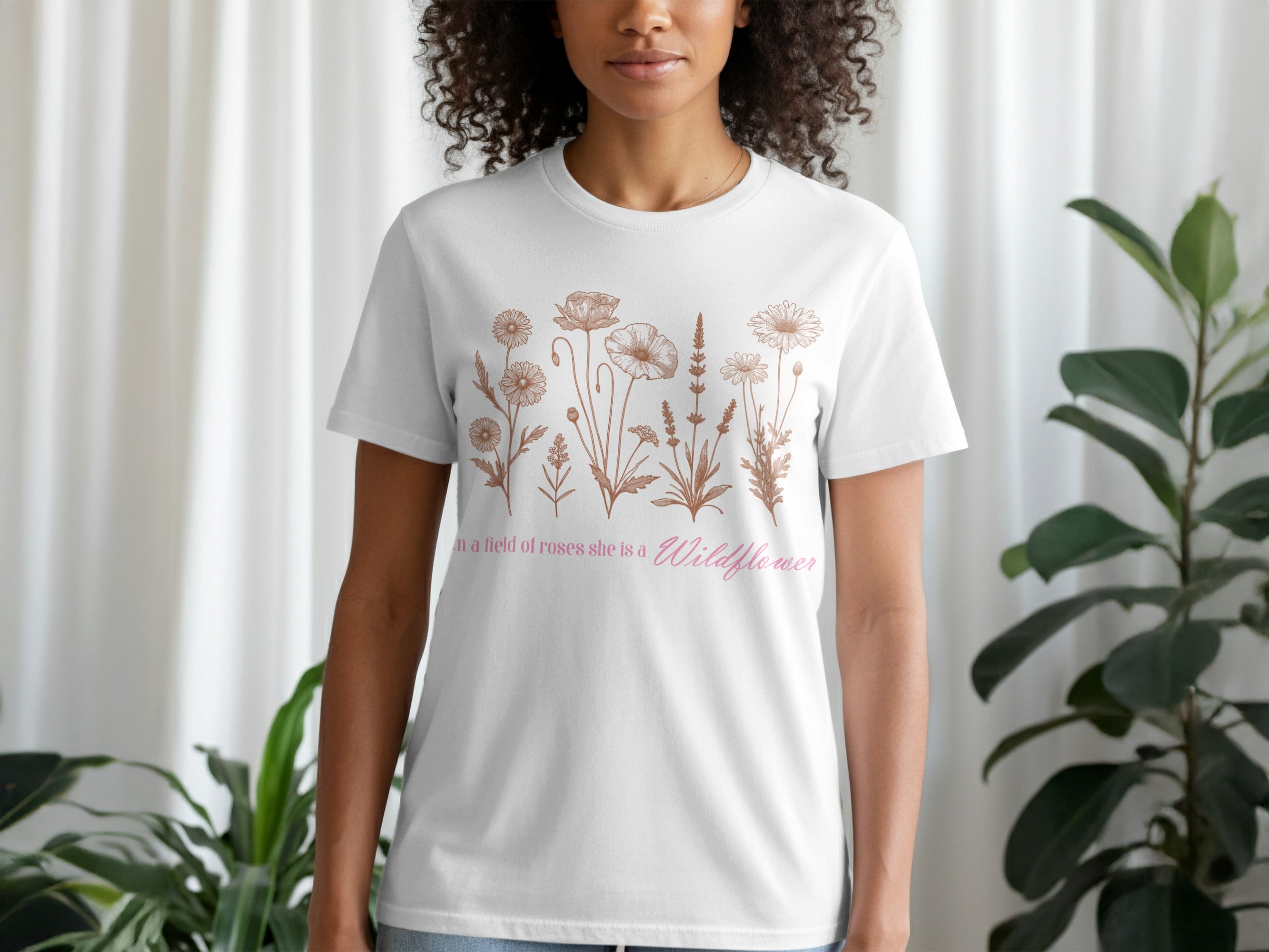 White t-shirt with line drawing of wildflowers and text "in a field of roses she is a Wildflower".