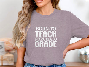 T-shirt with white text "BORN TO TEACH FORCED TO GRADE".