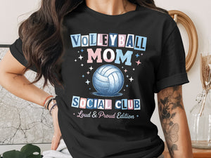 A person wearing a black t-shirt printed with "VOLLEYBALL MOM SOCIAL CLUB Loud & Proud Edition".