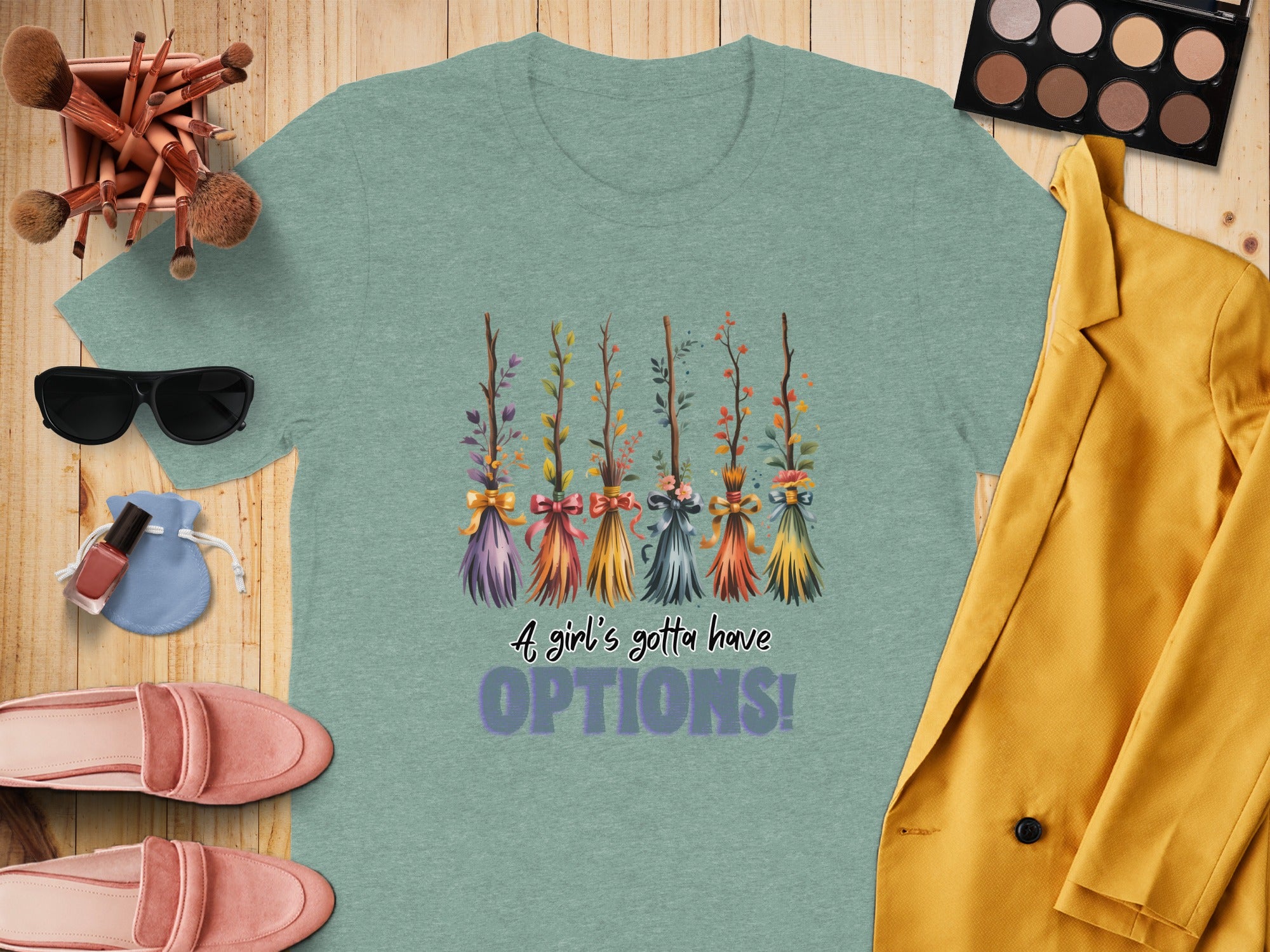 Green t-shirt with five decorative witch brooms and text "A girl's gotta have OPTIONS!"