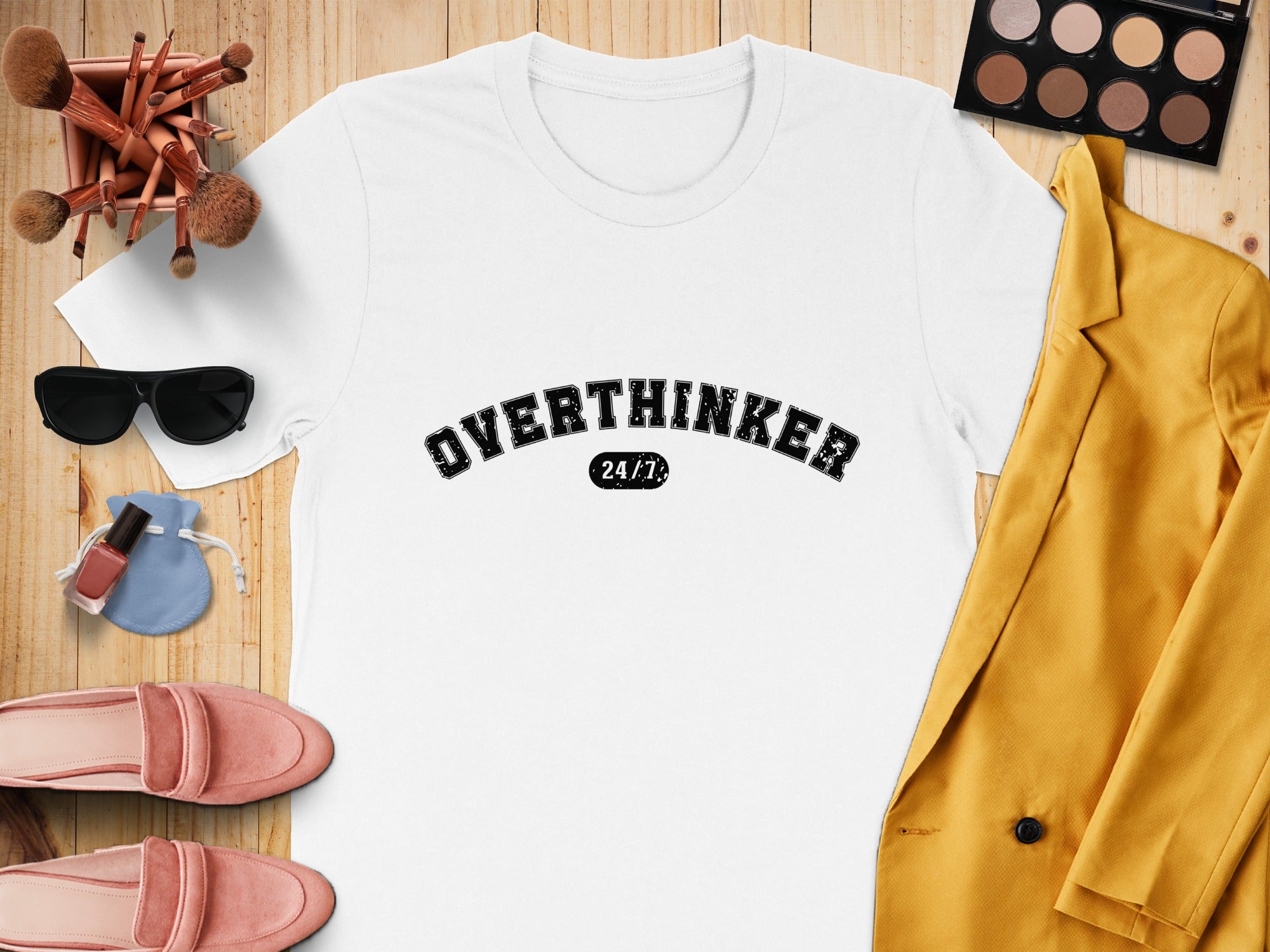 White t-shirt with "OVERTHINKER 24/7" text, arranged with makeup brushes, sunglasses, and a yellow blazer.