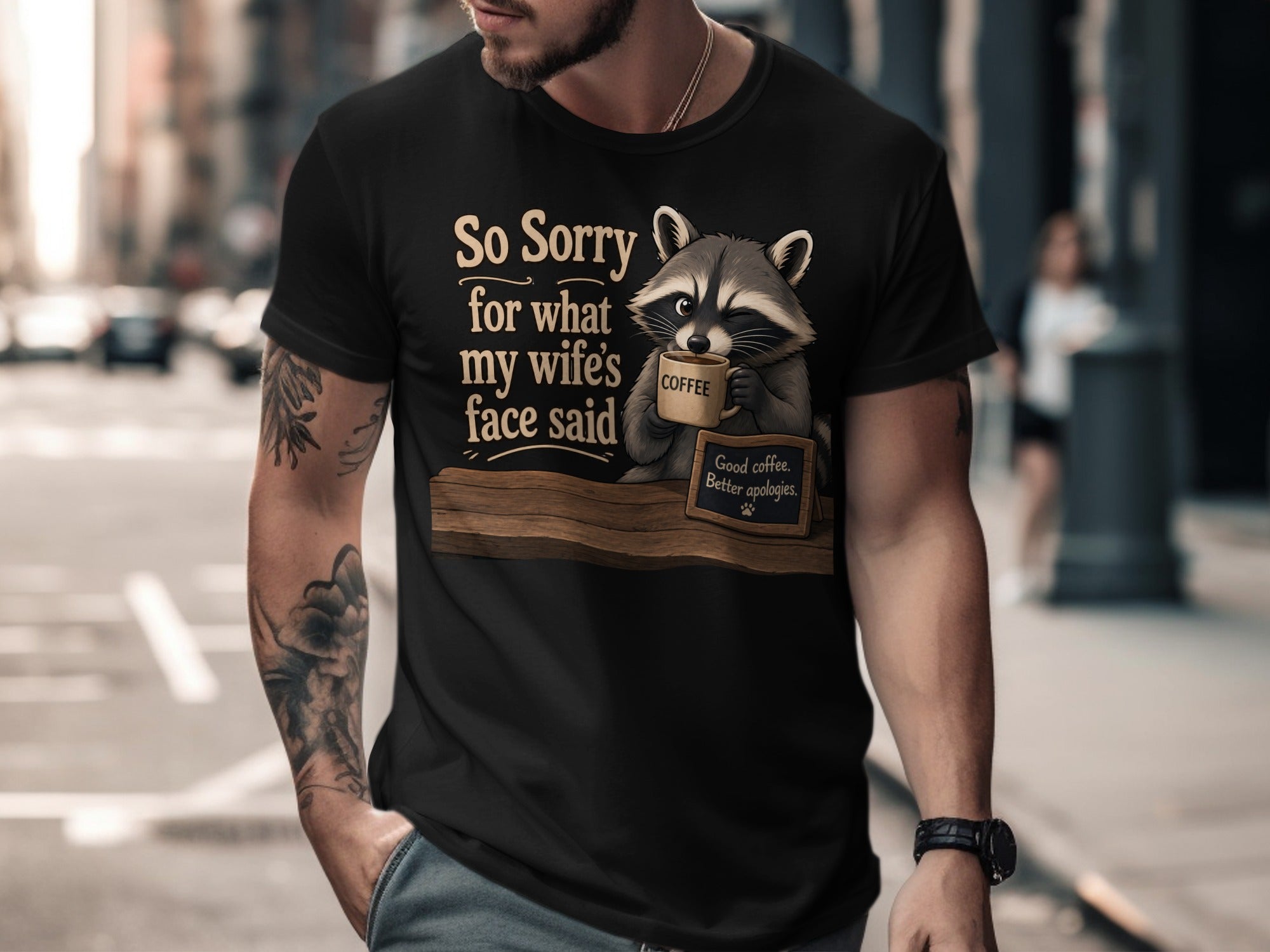 T-shirt graphic with raccoon holding coffee and text: "So sorry for what my wife's face said."