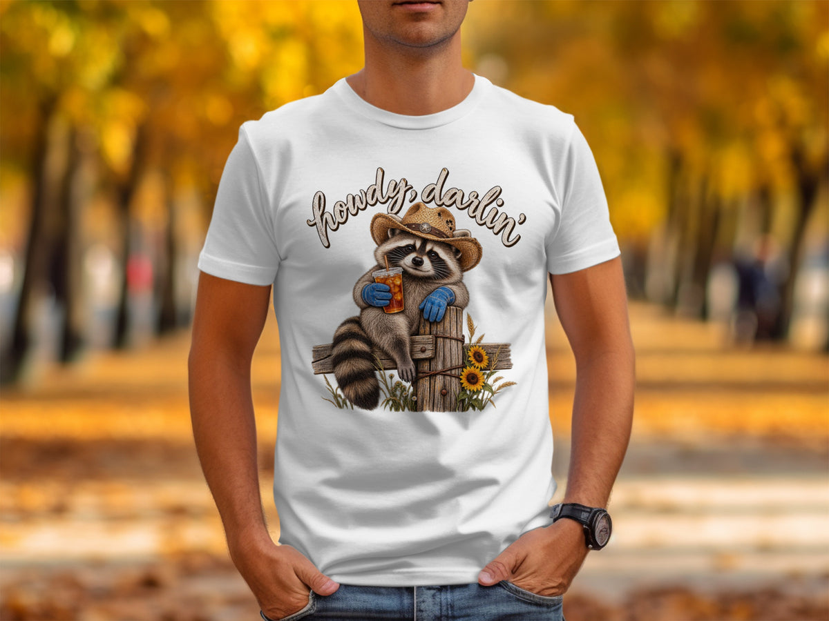 White t-shirt with a raccoon in a cowboy hat and the words "howdy darlin'".