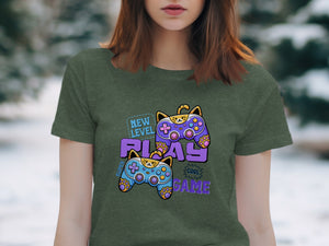 Green t-shirt with purple and blue cat-shaped game controllers and "NEW LEVEL PLAY COOL GAME" text.